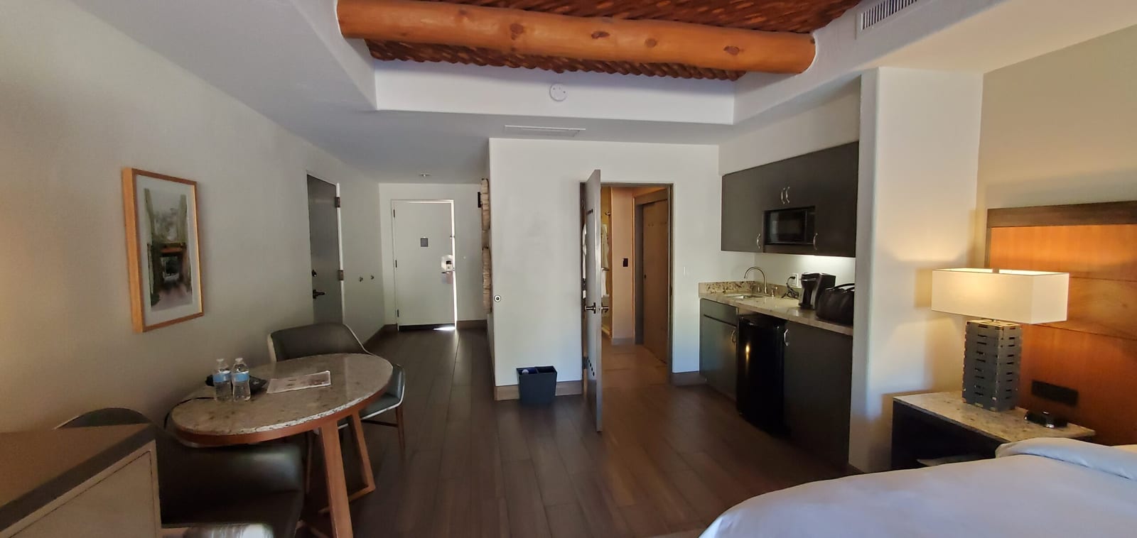 Open-concept layout showcasing exposed timber vigas, plush king bed, and natural desert daylight. Signature Casita interior panorama with authentic viga and latilla wood ceiling